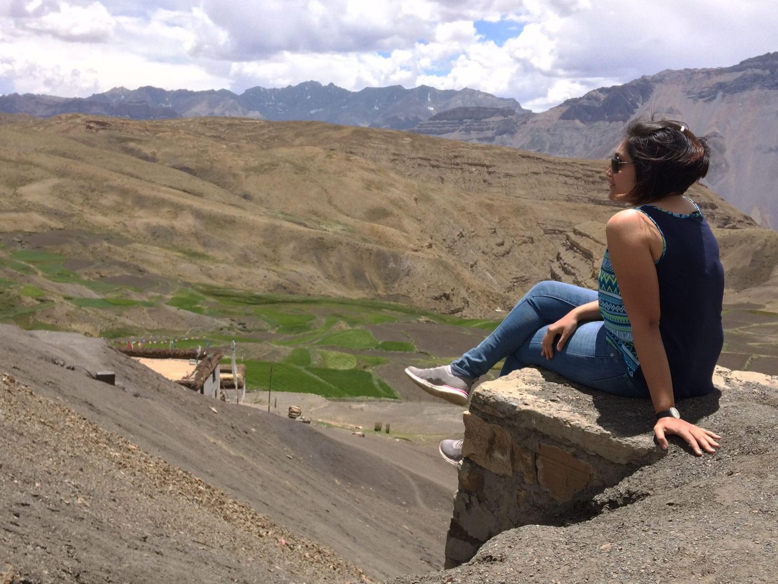 Shyama sitting on a rock ledge above the fields of Kibber